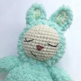 Close view of bunny amigurumi head with embroidered face, calm expression and fluffy handmade texture
