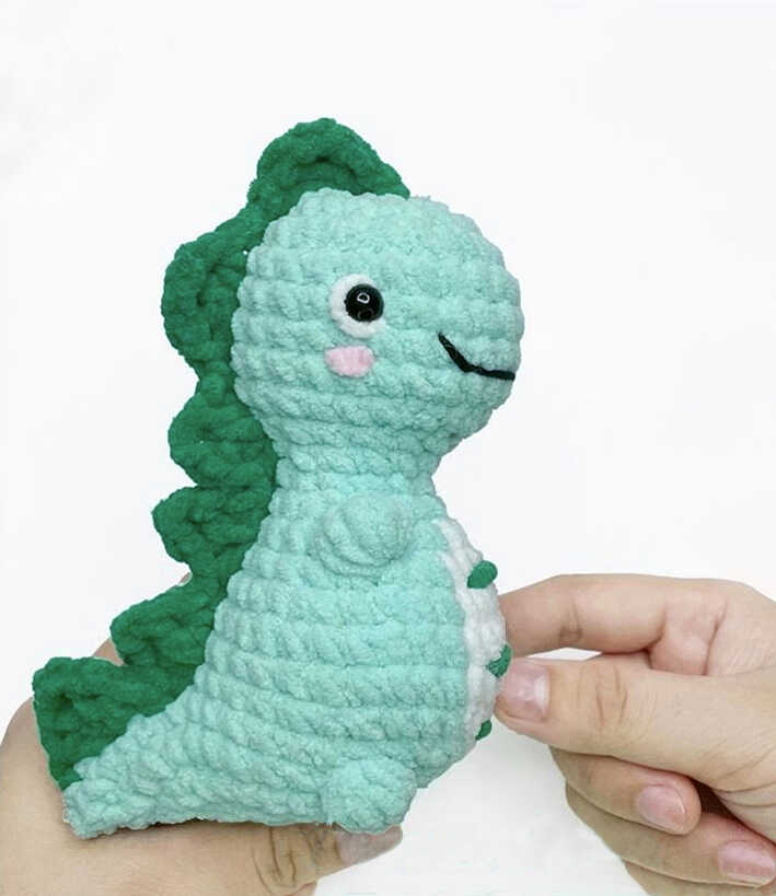 Handheld no sew dinosaur amigurumi showing size scale, soft plush texture and neat crochet shaping